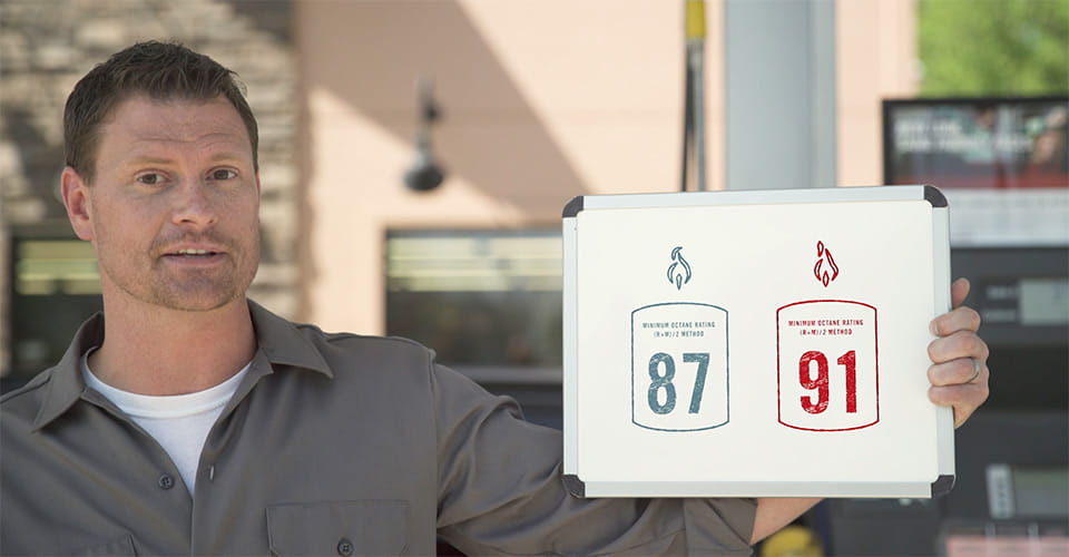 Man holding sign showing minimum octane ratings of 87 and 91