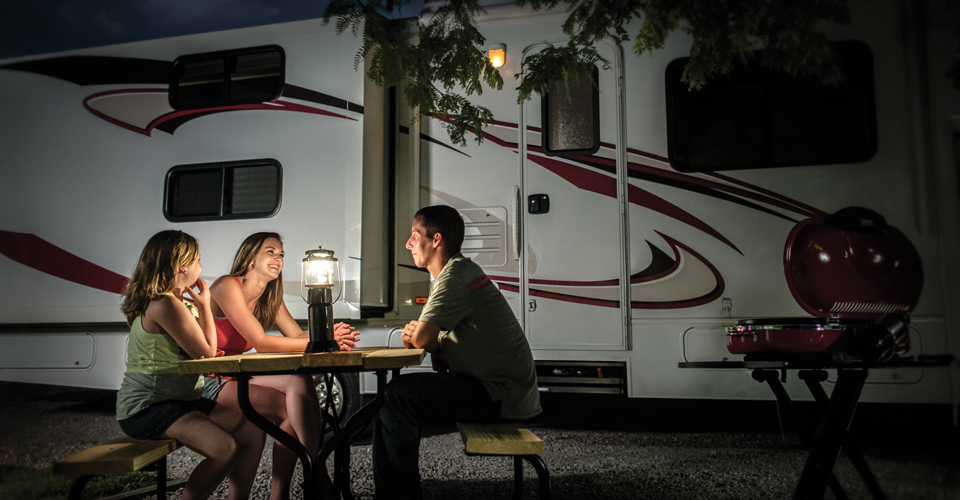 Family sitting a picnic table at night with the light of a lantern