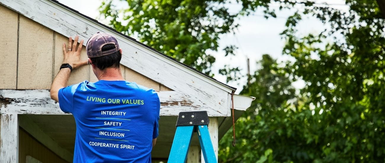 A man standing up on a ladder next to a building. 