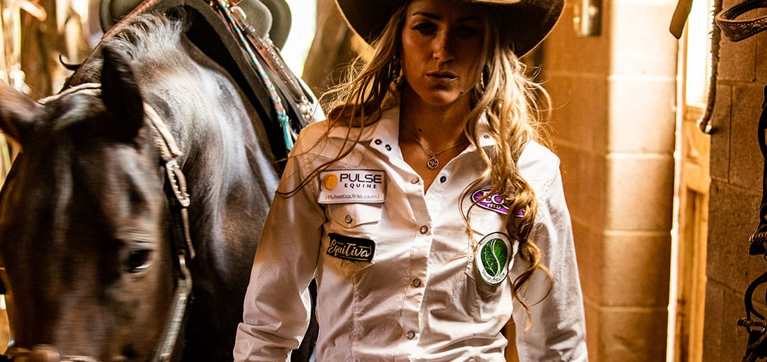 Focused cowgirl walking out of stable with horse