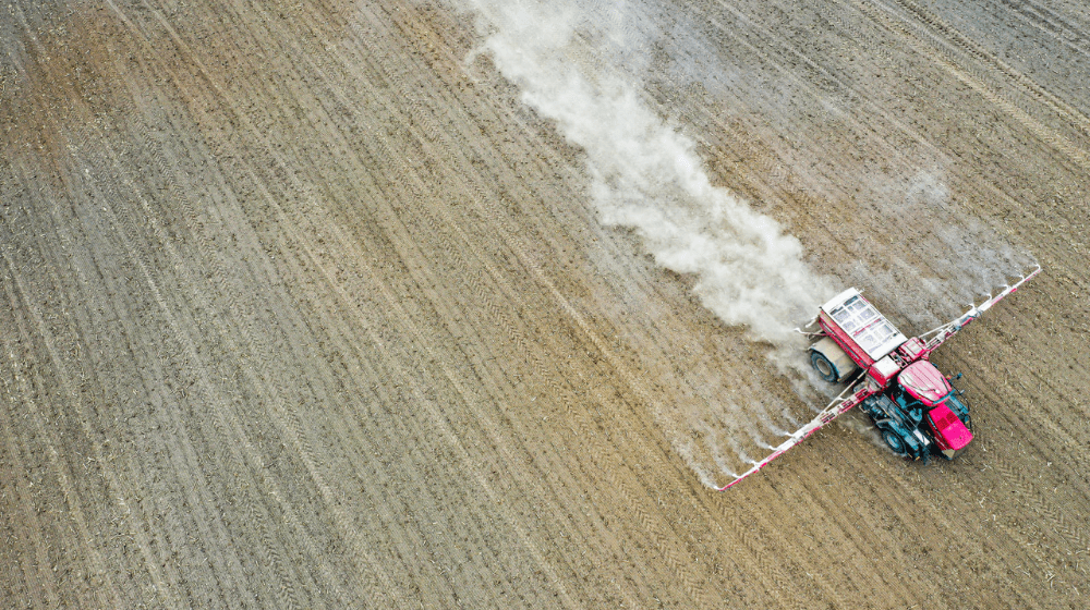 Aerial view of a tractor spreading material across a dry field