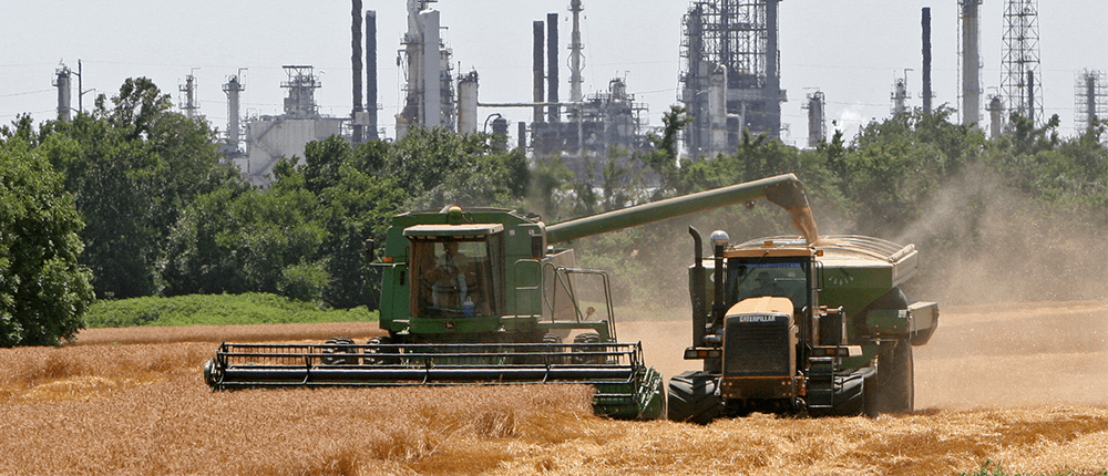 Farm equipment in field in front of refinery