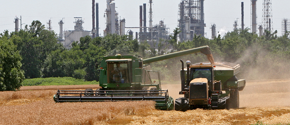 Farm equipment in field in front of refinery