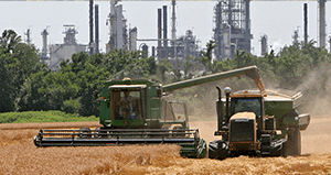 Farm equipment in field with refinery in background