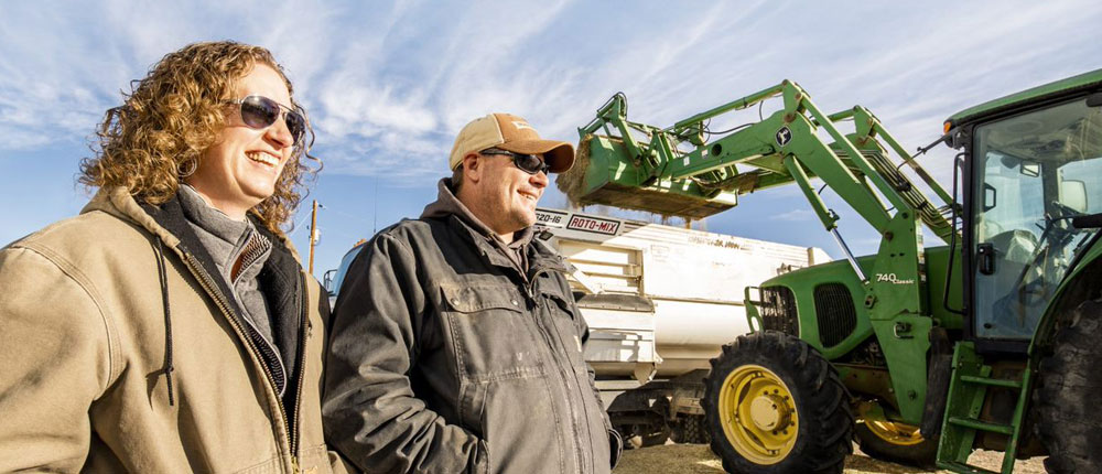 A photo of Brandy and Kevin Evans with a tractor loading a truck full of calf feed in the background.
