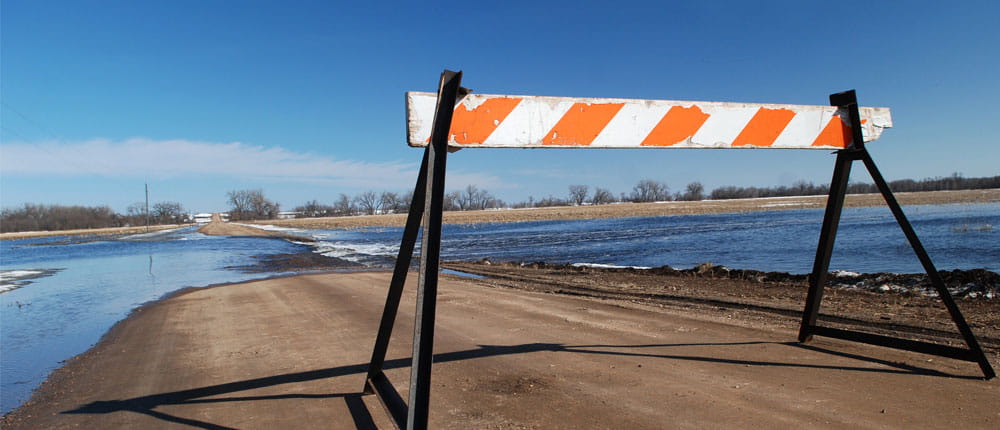 A roadblock sign prevents cars from traveling over flooded roads.
