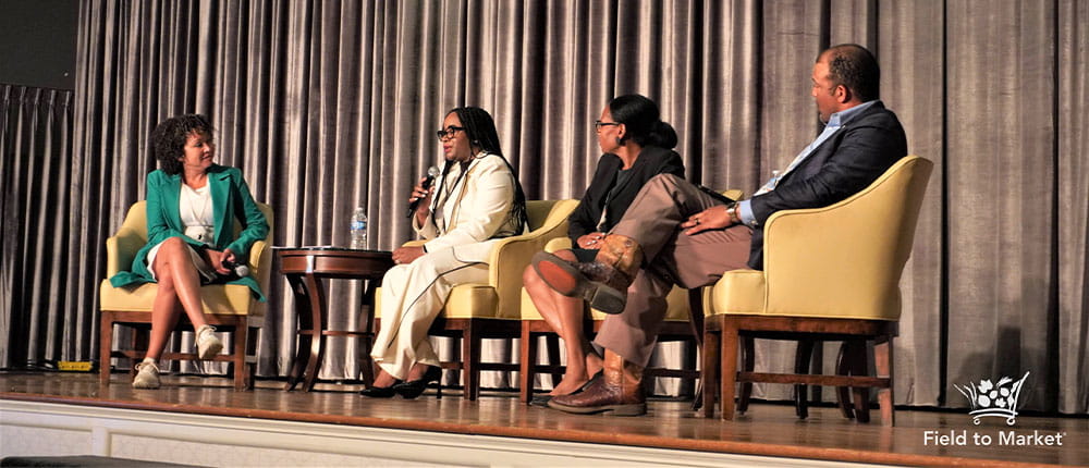 Four people on stage seated in chairs, with curtain behind them