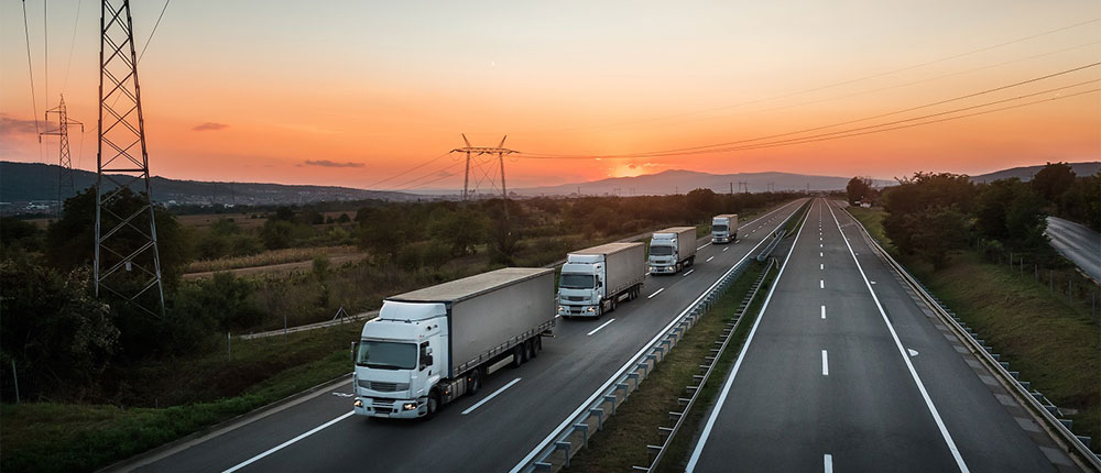 Four semis driving on a road at sunset