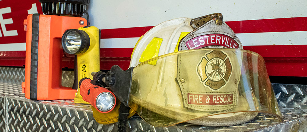 Close-up of a helmet with face shield and helmet-mounted flashlight, along with two other handheld flashlights