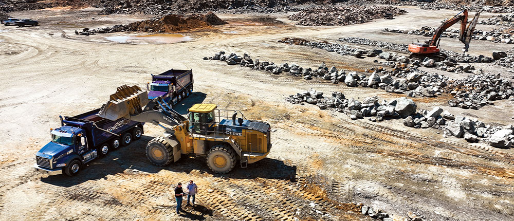 An end loader dumps rock into a dump truck in a rock quarry.