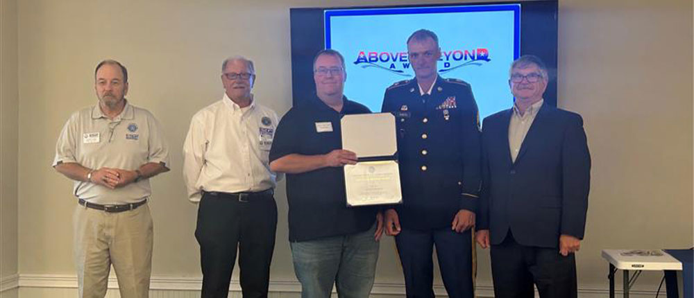Five men in front of a TV screen that depicts the Above and Beyond Award logo