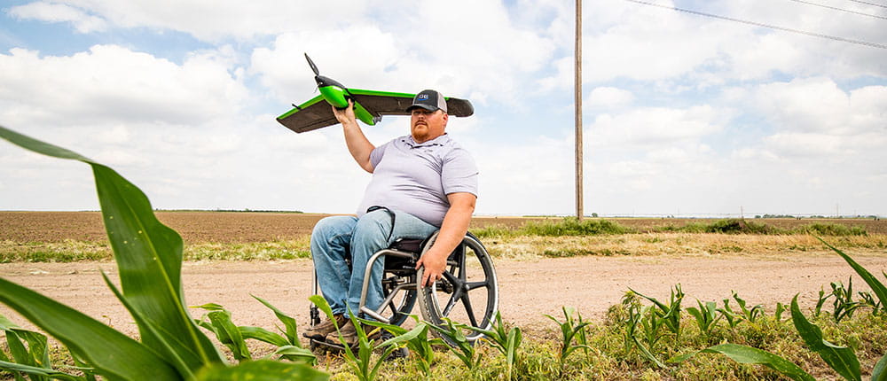 Man in wheelchair gets ready to launch a drone over farm fields.