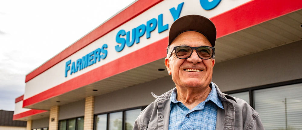 Man standing in front of building that says Farmers Supply Cooperative on the outside