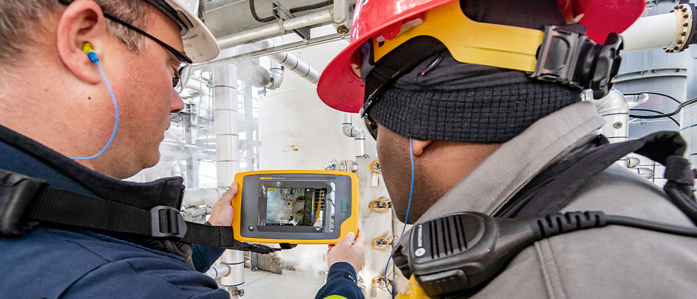 Two men wearing safety gear looking at a hand-held tablet-sized video screen