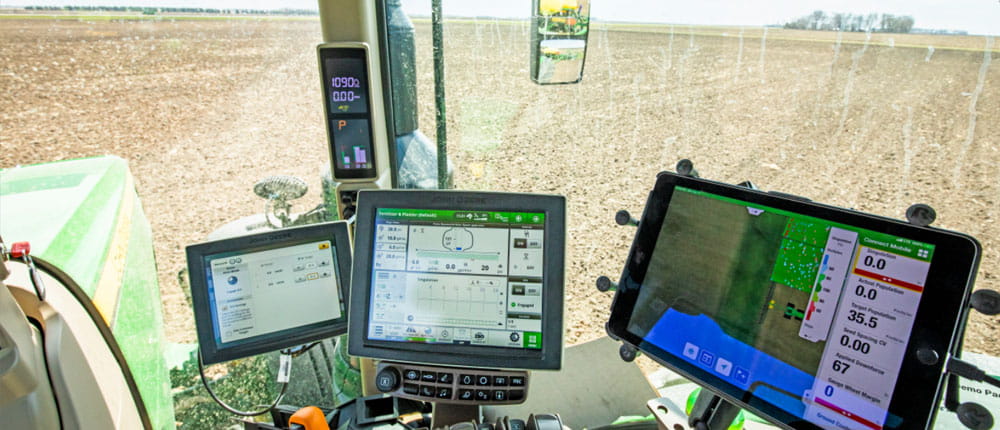 Inside a tractor looking at screens displaying data from precision agriculture software 
