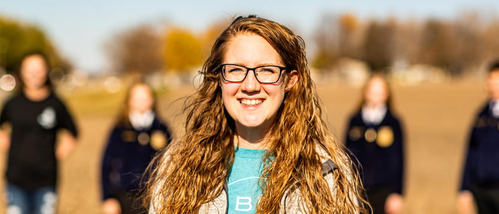 A teacher standing in a field with students in the background. 
