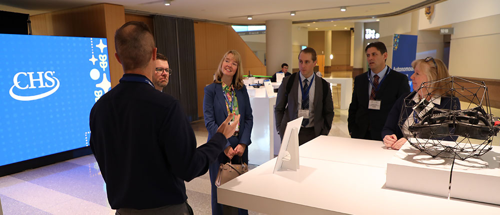 People looking at a drone, with the CHS logo on a screen in the background