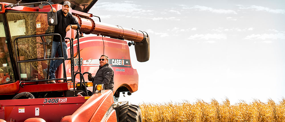 Two men on a tractor with corn field in the background