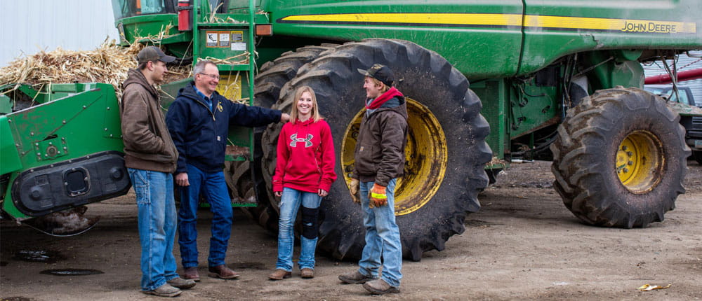 A few people stand in front of a combine smiling