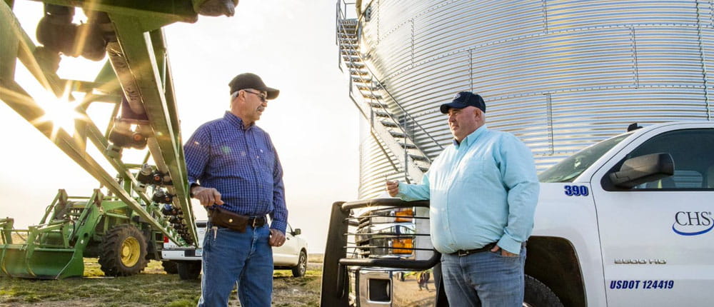 Farmer and agronomist talking near farm equipment and grain bin
