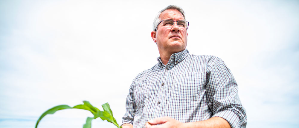 A farmer stands at the edge of a barn looking out onto his fields.