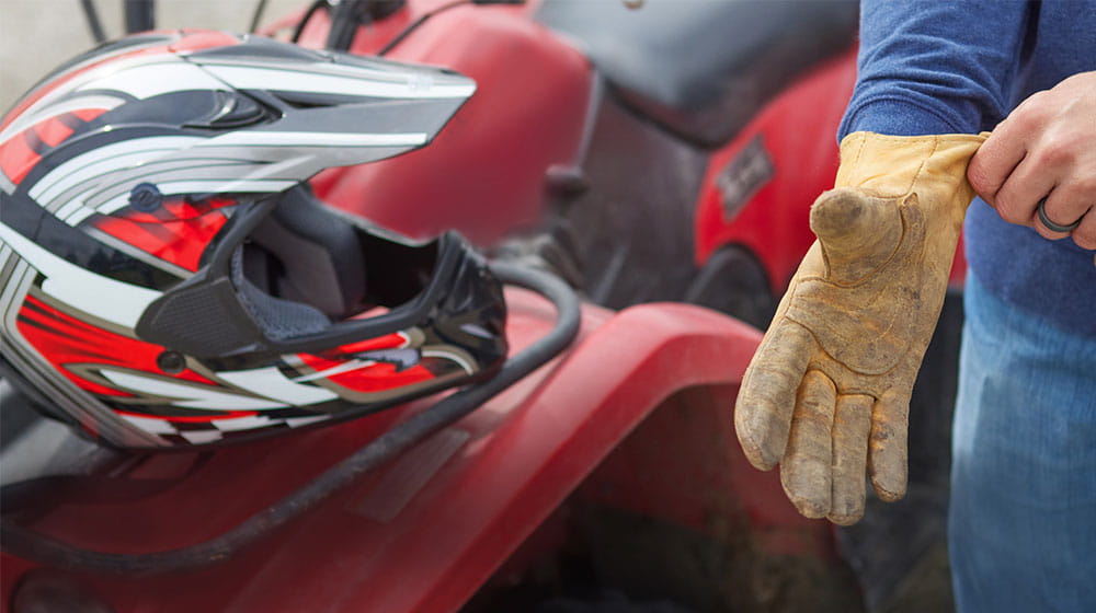Safety helmet resting on ATV and man pulling on glove