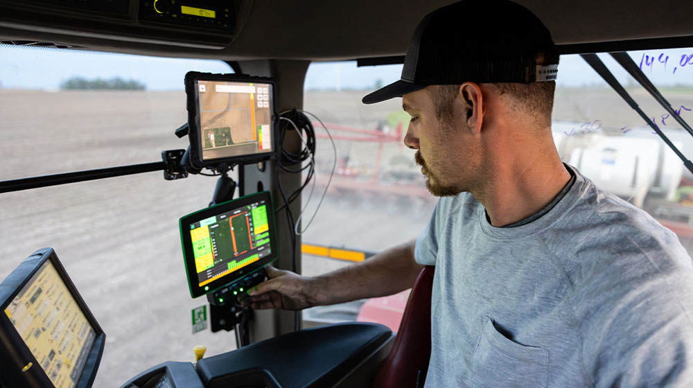 Man sitting inside tractor looking at technology screens showing graphs