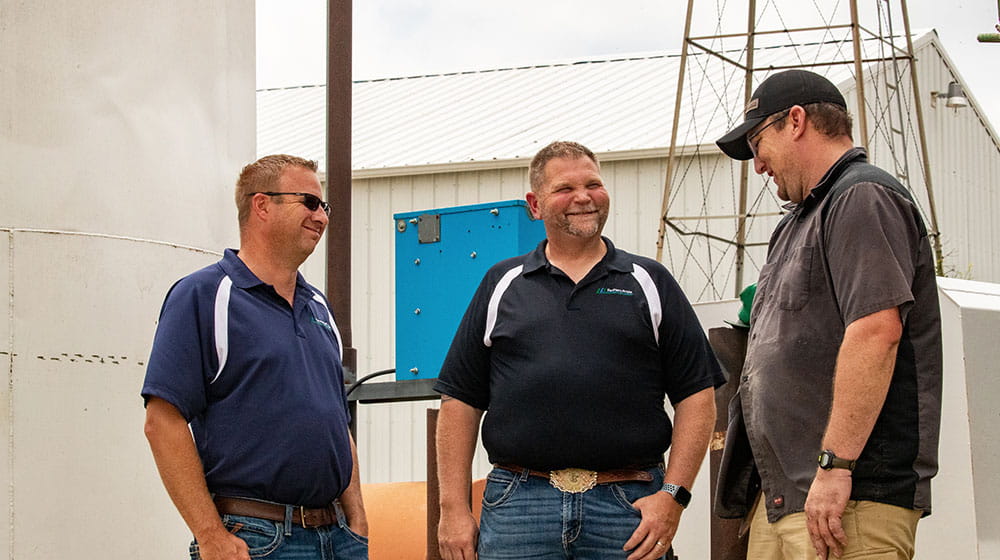 Three men talking outside on a farm.