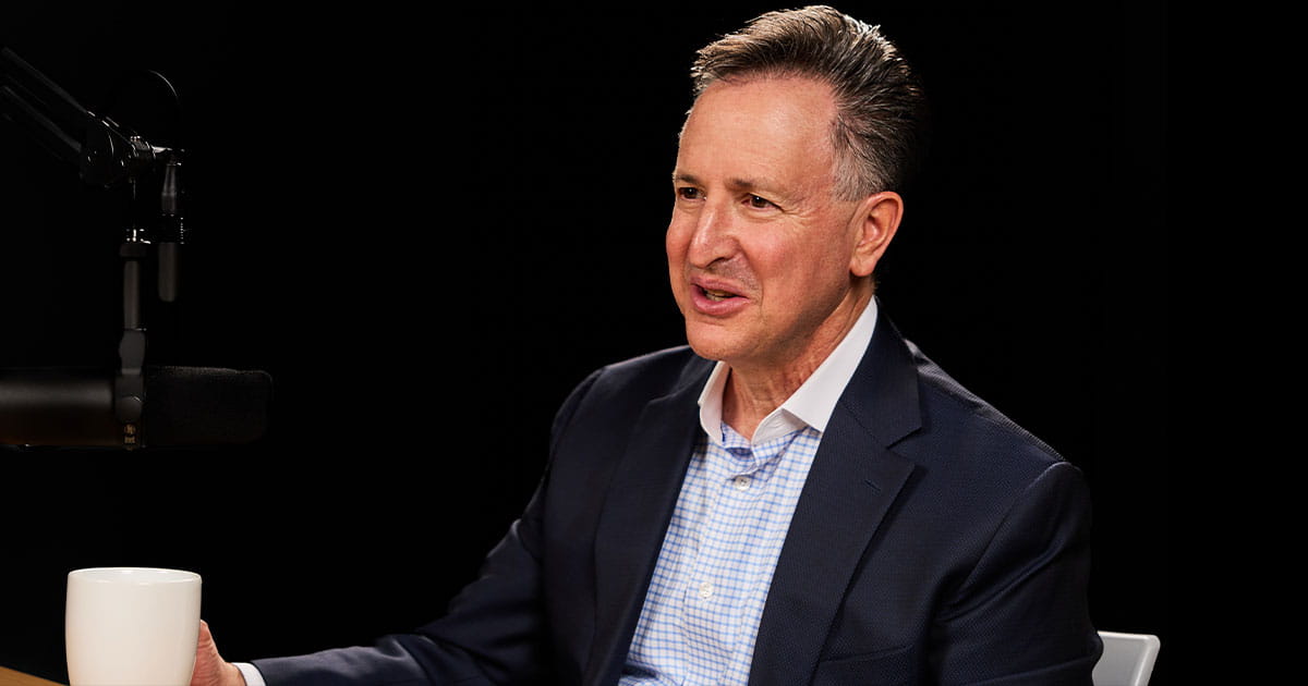 Man sitting in a studio beside a microphone and holding a coffee mug
