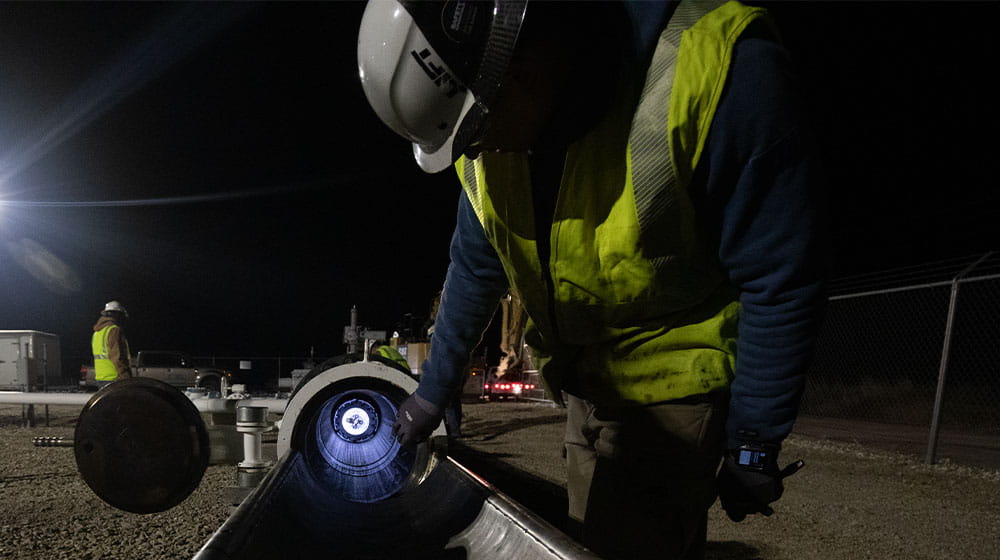Man wearing yellow safety vest and hard hat checking a pipeline that contains a smart pipeline inspection gauge at night