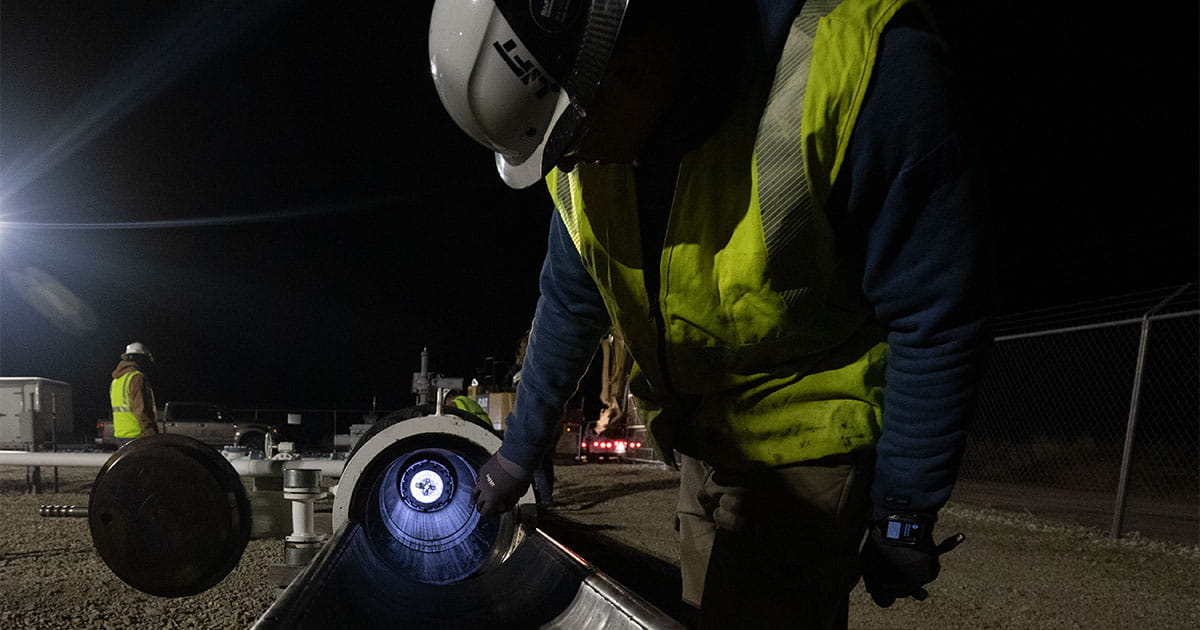 Man wearing yellow safety vest and hard hat checking a pipeline that contains a smart pipeline inspection gauge at night