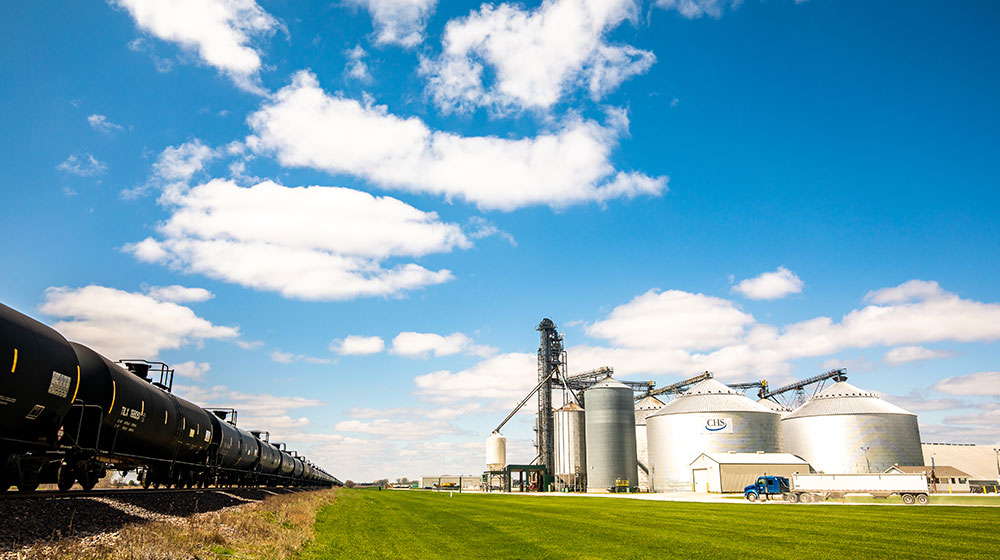 Grain bins beside a railroad track under a cloudy blue sky