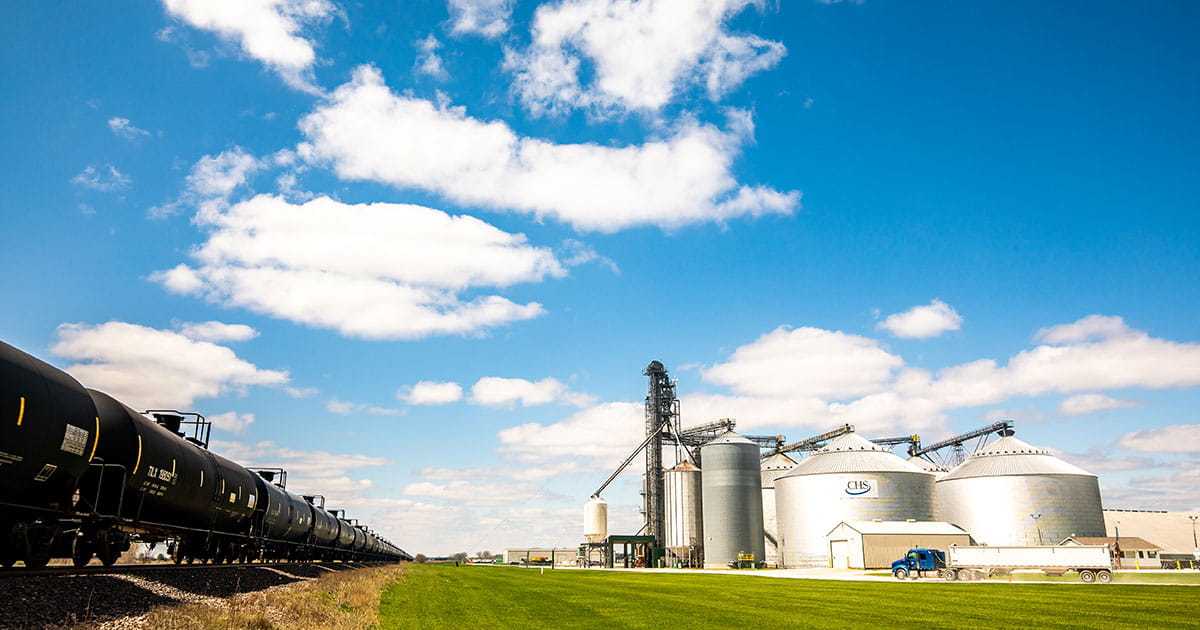 Grain bins beside a railroad track under a cloudy blue sky 