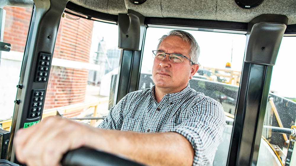 A man sitting inside a tractor cab with hands on wheel