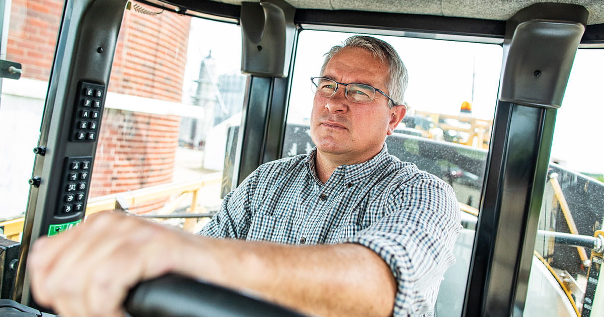 A man sitting inside a tractor cab with hands on wheel