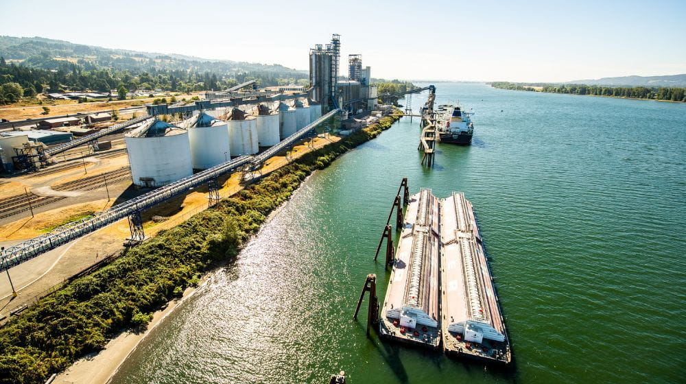 Aerial view of a grain terminal with silos and barges loading along a river.