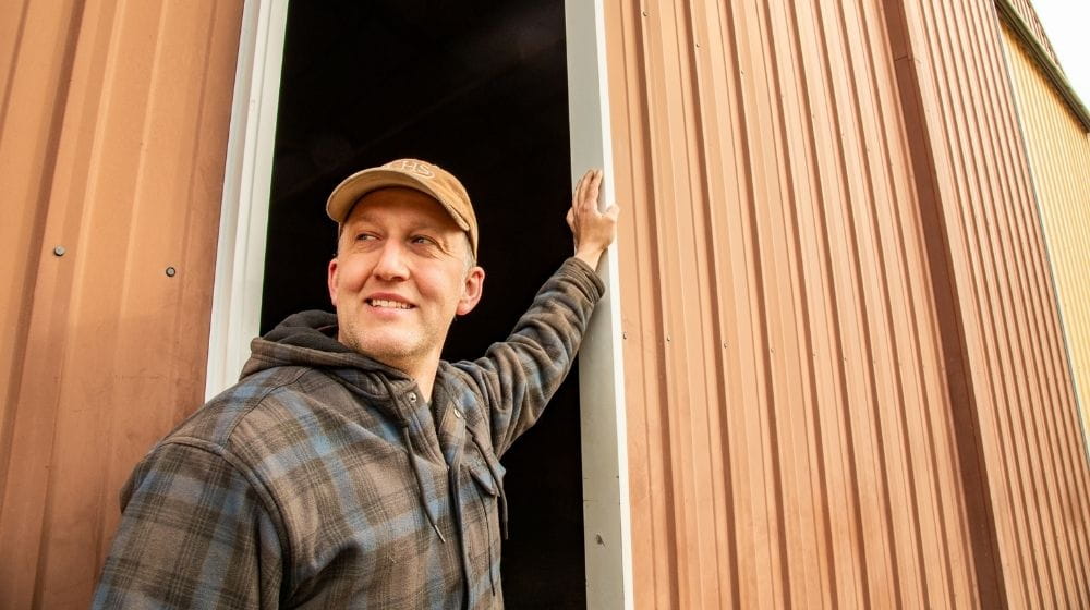 Man in hat in front of machine shed